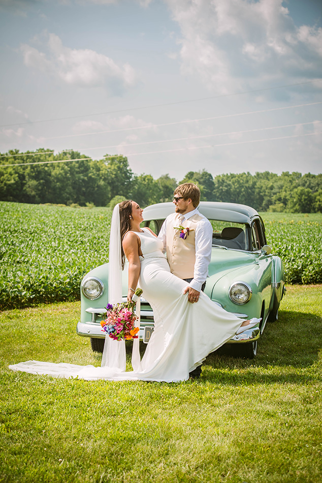 Couple posing beside a vintage car, capturing timeless elegance on their wedding day.