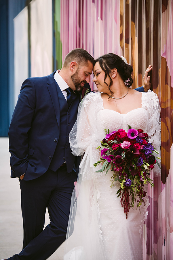 Bride and groom snuggled up against a vibrant wall mural, creating a playful and intimate portrait.